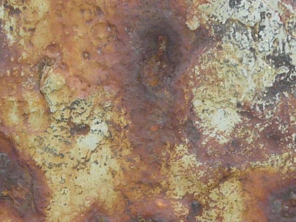 Rusted metal texture, formed into a rough, uneven surface in various hues of blue, yellow and red.